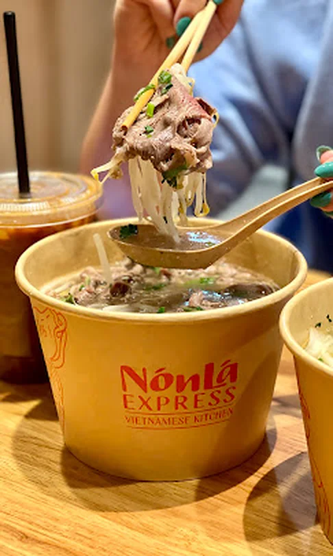 Chopsticks lifting silky rice noodles and beef from a Nón Lá Express phở bowl