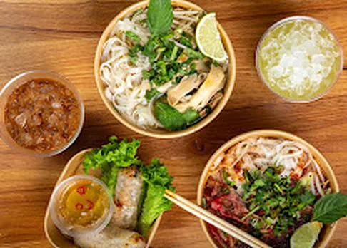 Top-down spread of chicken phở, spicy phở, summer rolls and iced drinks from Nón Lá Express in Flushing NY